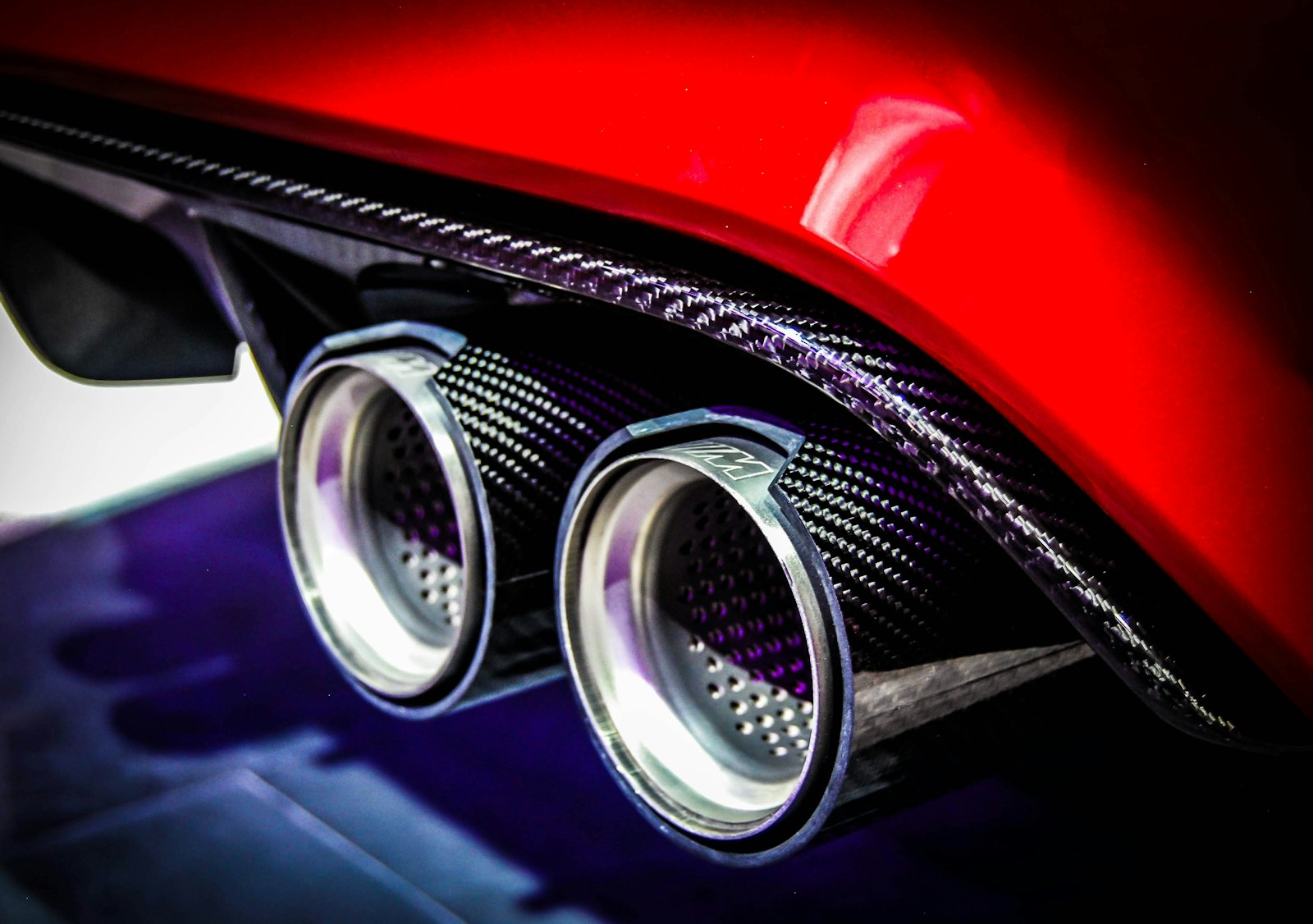 Twin chrome exhaust tips on a red performance car with carbon-fibre diffuser